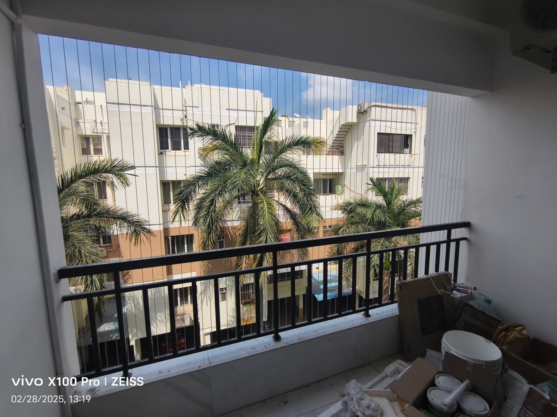 Balcony with black railings fitted with vertical invisible grill cables overlooking palm trees in a Chennai apartment community