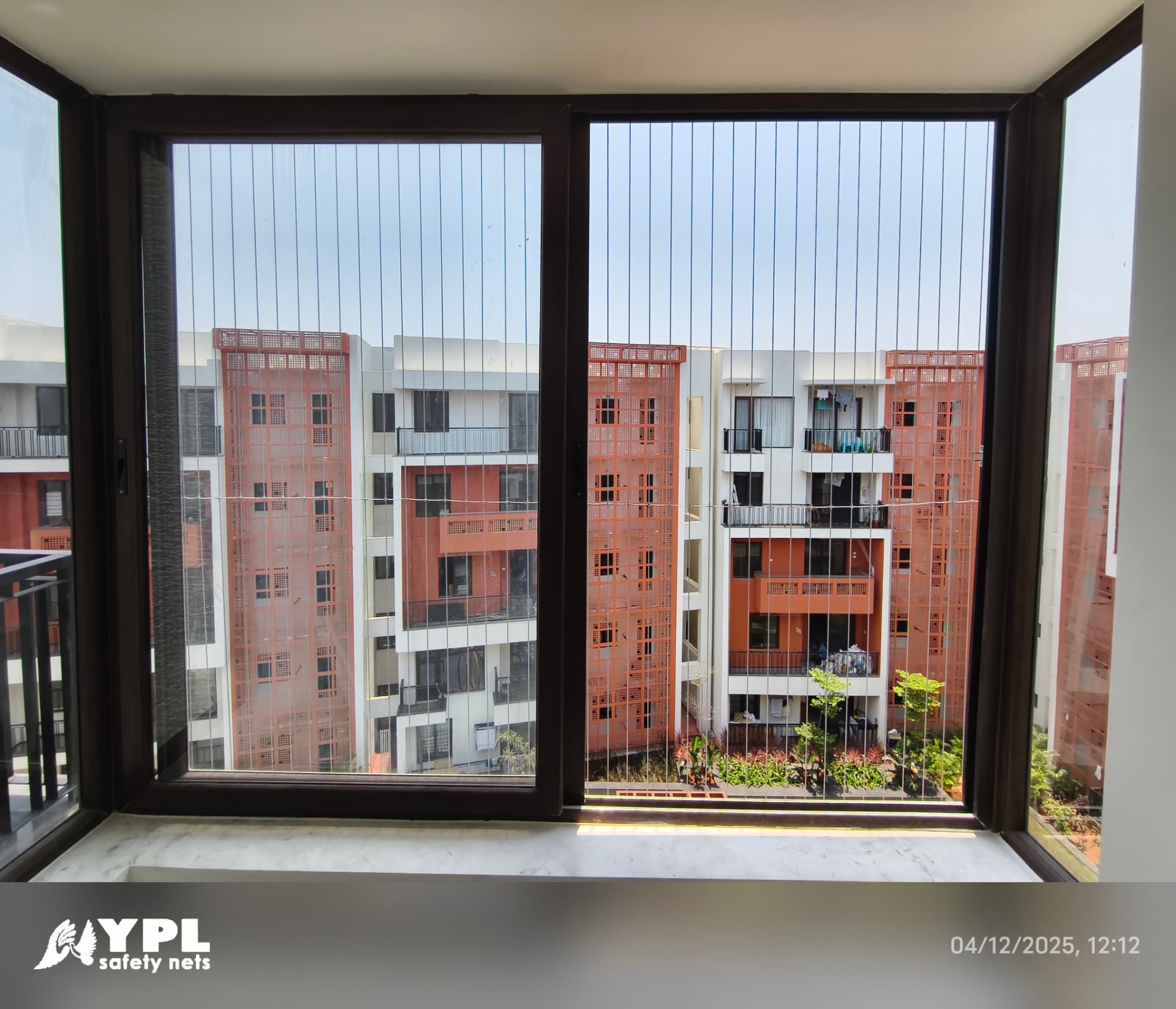 Large sliding window and balcony door fitted with vertical invisible grill cables facing an apartment complex in Chennai