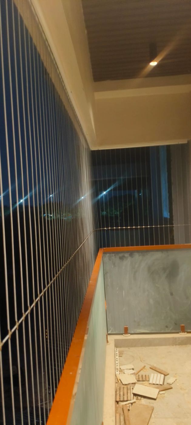 Vertical invisible grills enclose a narrow balcony with orange-edged parapets and an unfinished floor at night.