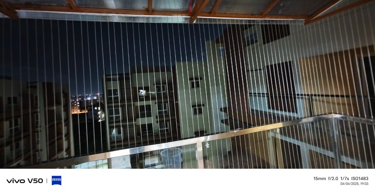 Vertical invisible grills enclose a covered balcony overlooking neighboring apartment buildings at night.