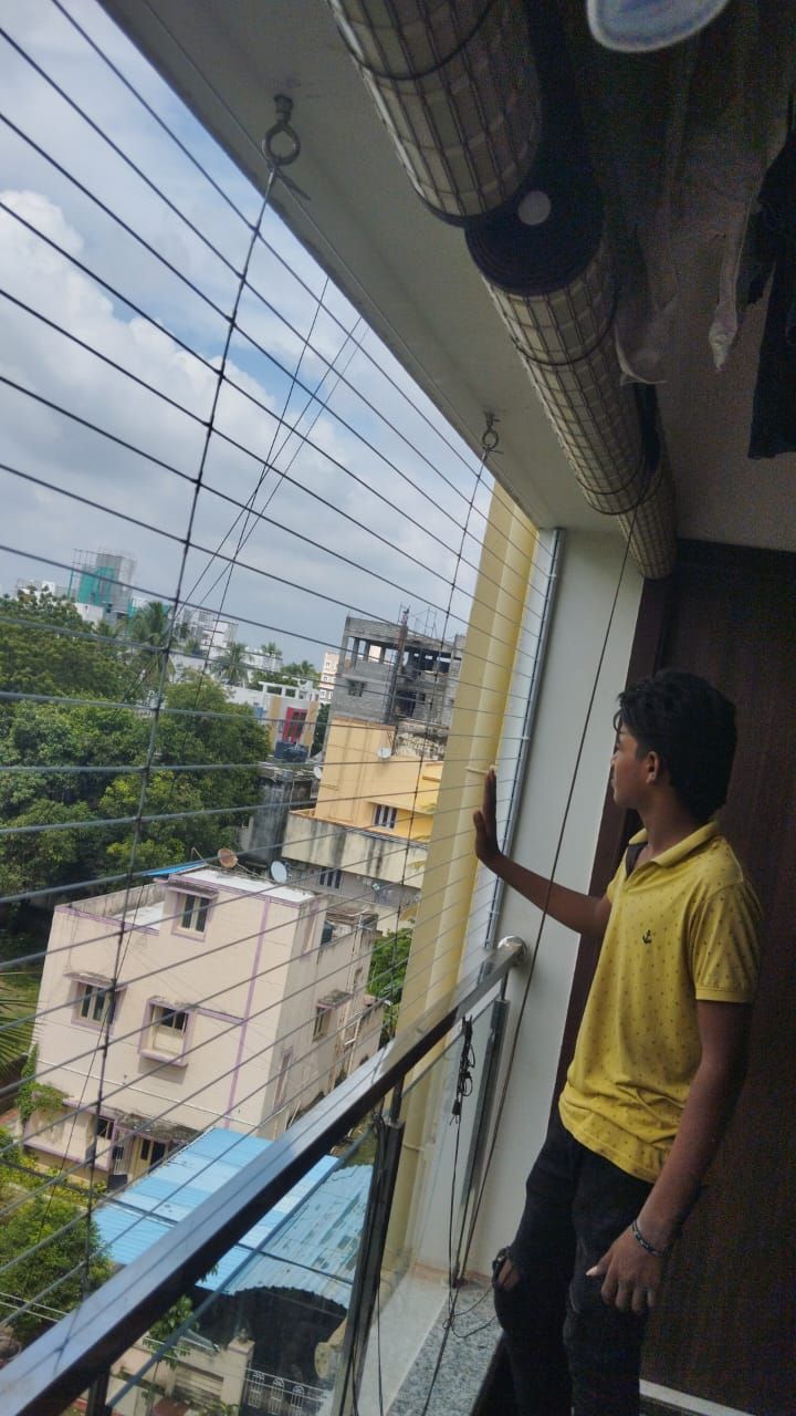 Man beside horizontal invisible grills at a wide window overlooking trees and nearby residential buildings.