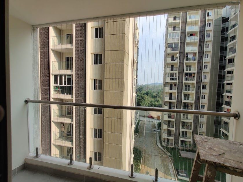 Apartment balcony with vertical invisible grills and glass railing facing neighboring high-rise towers and a courtyard driveway.