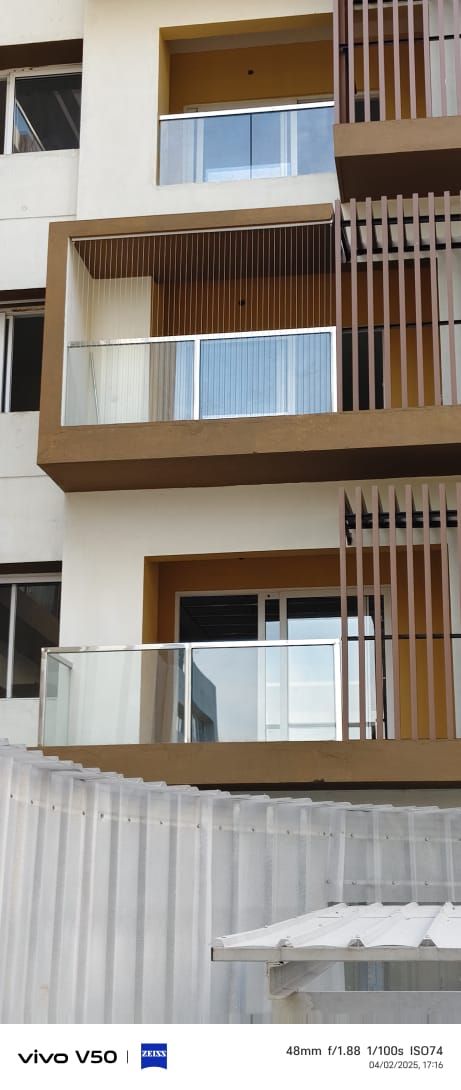 Apartment exterior with stacked glass-railed balconies, vertical invisible grills, and cream-and-brown facade detailing.