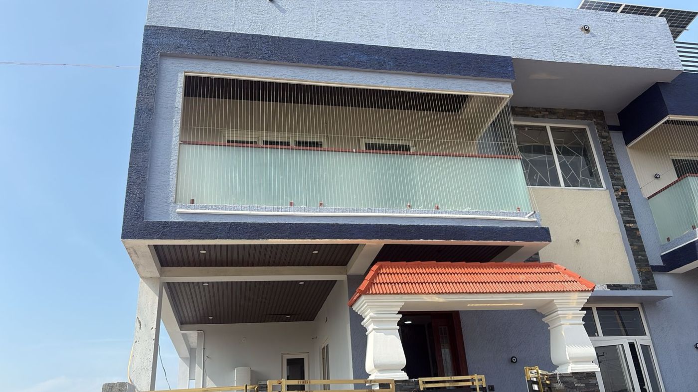 House exterior with vertical invisible grills enclosing an upper balcony above a tiled entrance canopy.