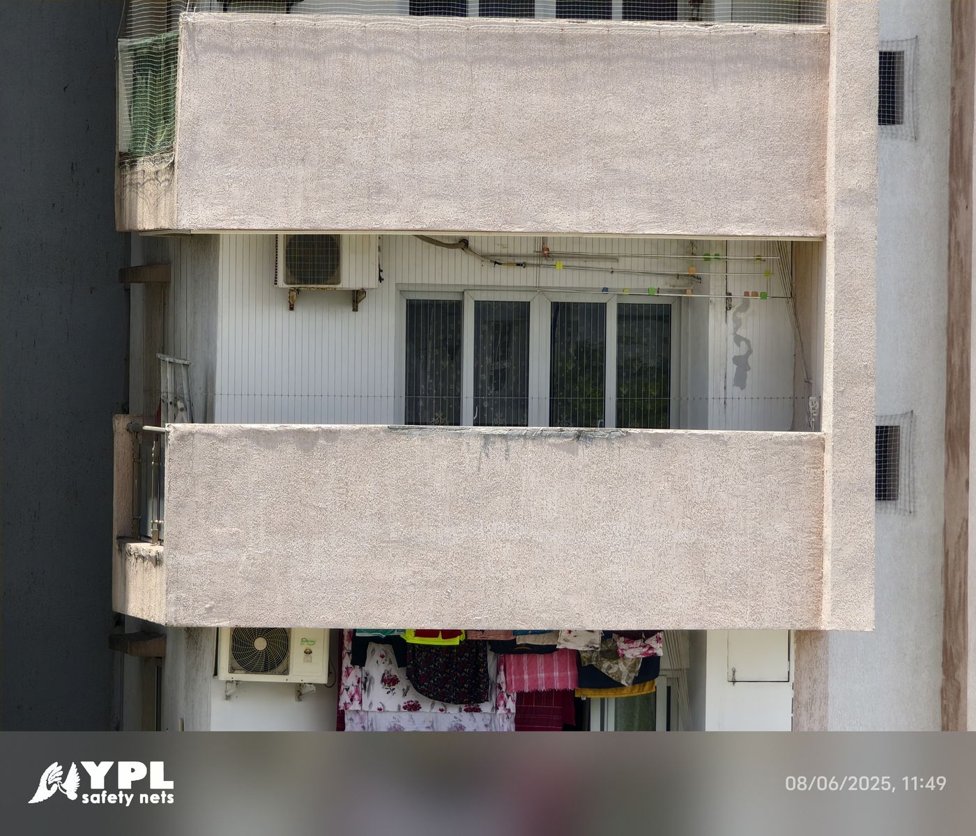 Apartment balcony enclosed with vertical invisible grills, with windows and an air conditioner behind a concrete parapet.