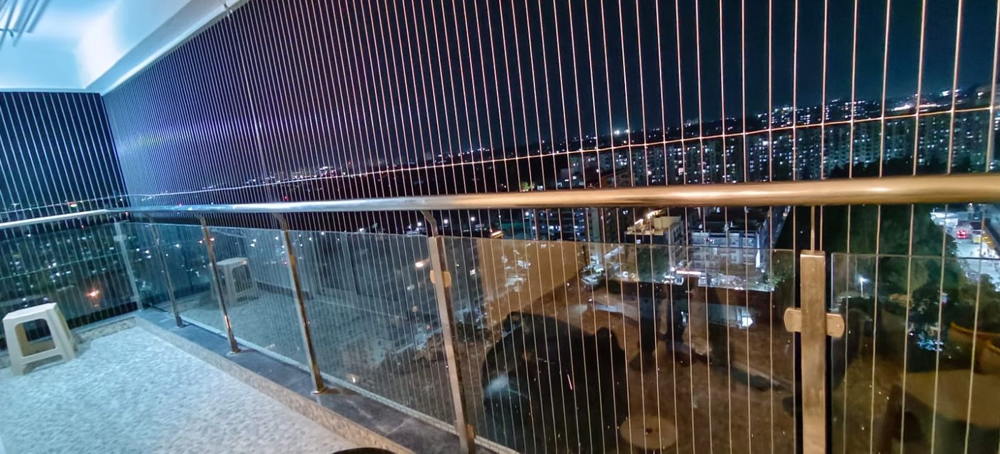 Balcony with vertical invisible grills and glass railing overlooking illuminated city streets at night.