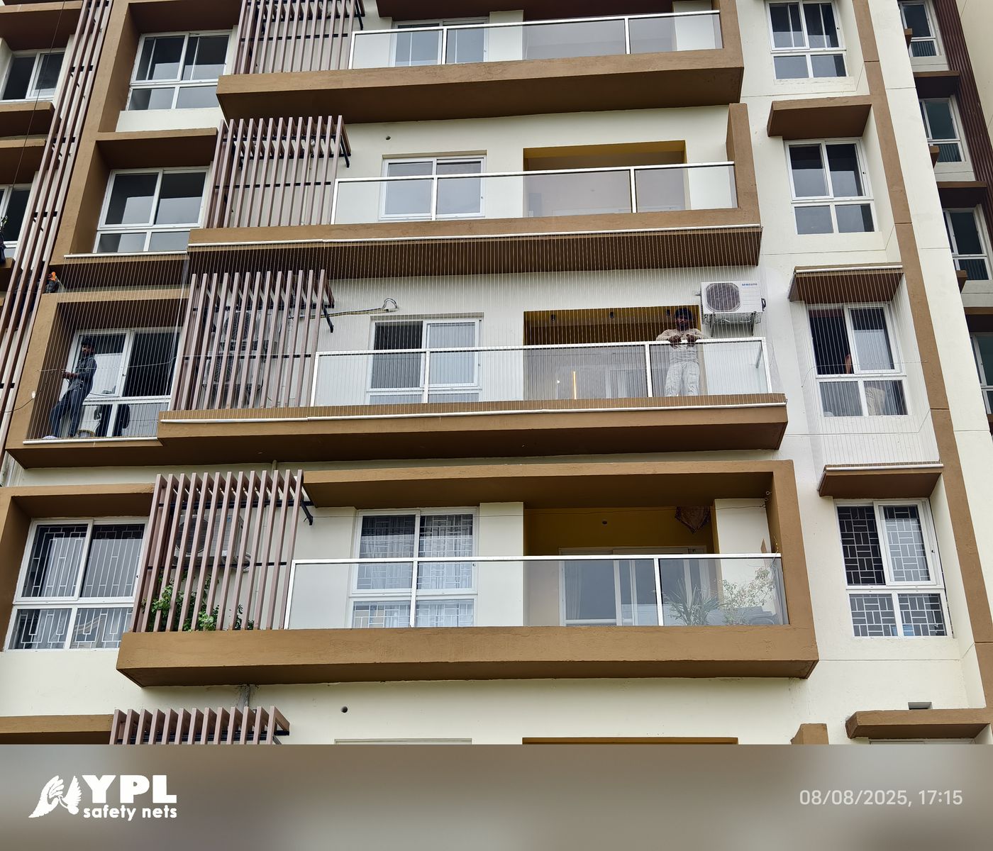Apartment building exterior with stacked glass-railed balconies, vertical invisible grills, windows, and air-conditioning units.