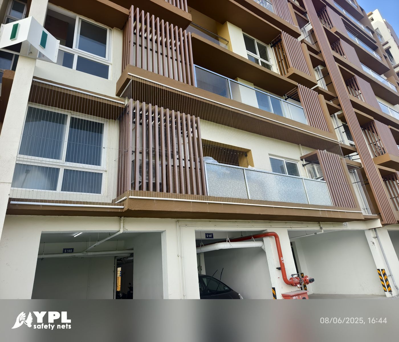 Apartment exterior with invisible grills across balconies and windows above ground-level parking.