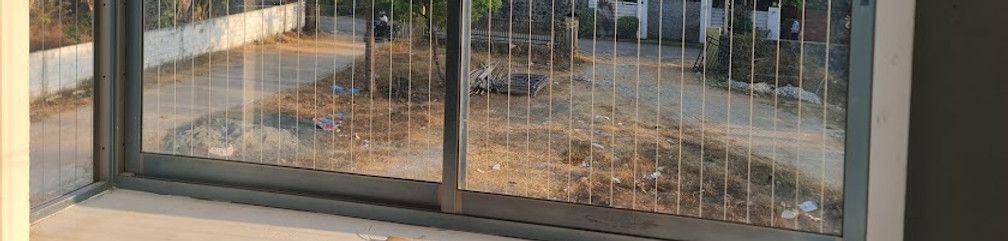 Close-up of lower sliding window frames and vertical invisible grill wires overlooking bare ground outside.
