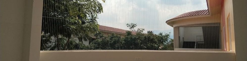 Vertical invisible grills across a balcony opening overlooking trees and neighboring tiled-roof homes.