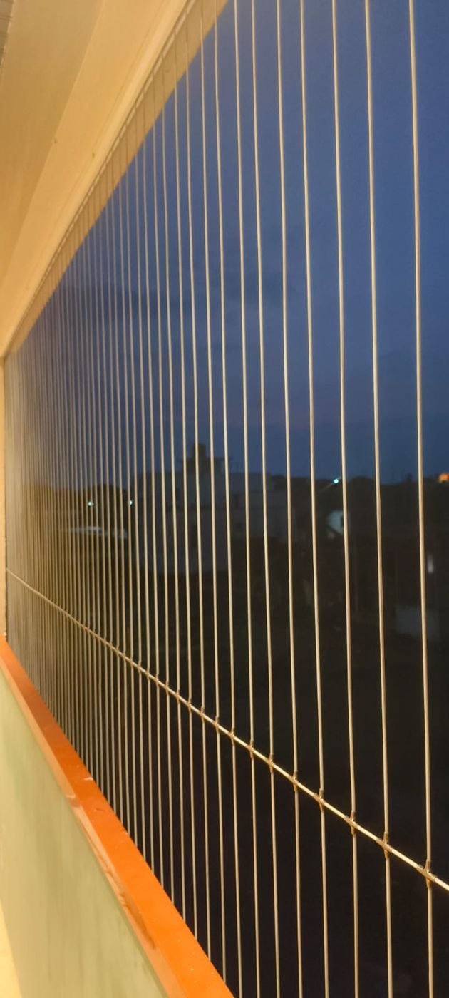 Close view of vertical balcony grill wires with horizontal supports against a dark evening sky.