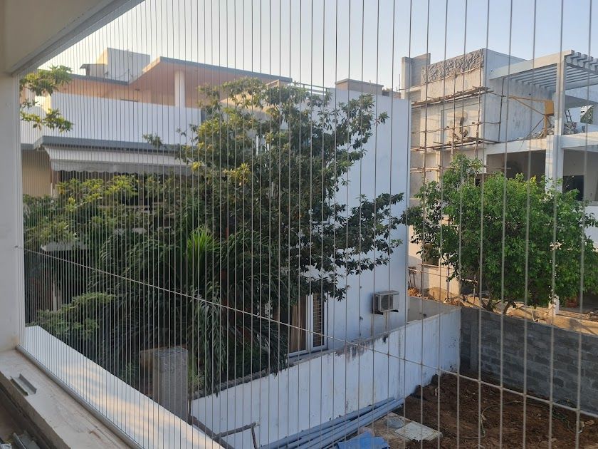 Balcony fitted with vertical invisible grills overlooking leafy trees and neighboring residential buildings.