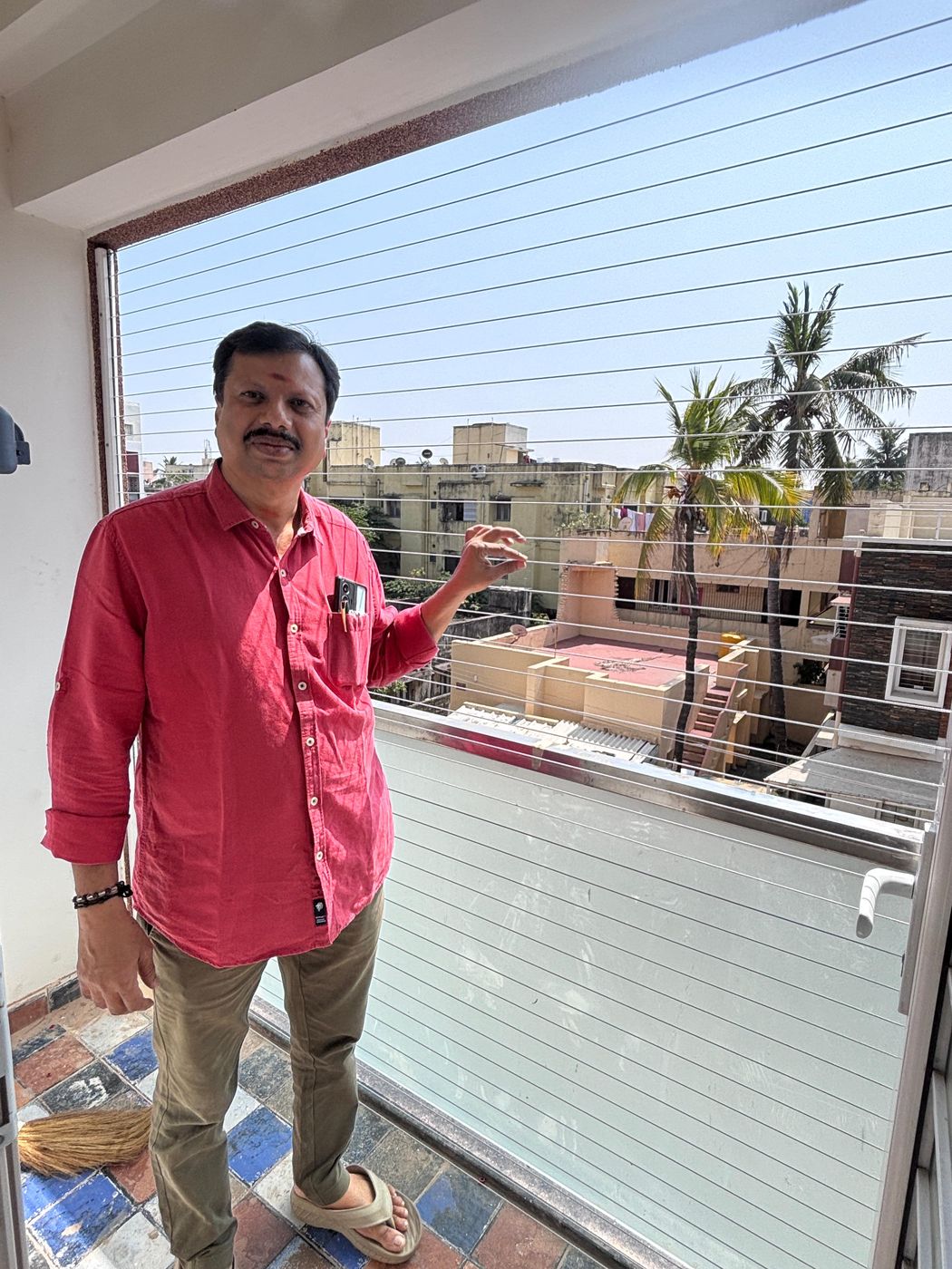 Man beside horizontal invisible grills across a large window opening overlooking rooftops and palm trees.