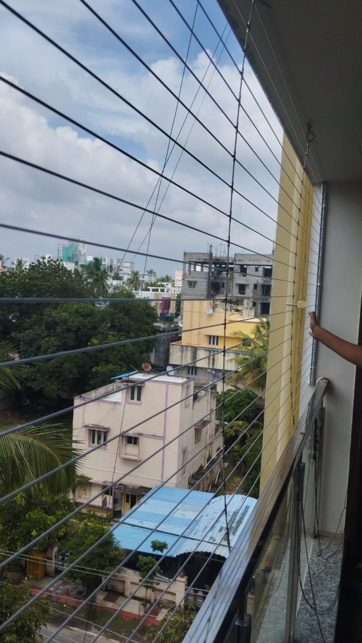 Balcony invisible grill overlooking trees and neighboring residential buildings beneath a cloudy sky.