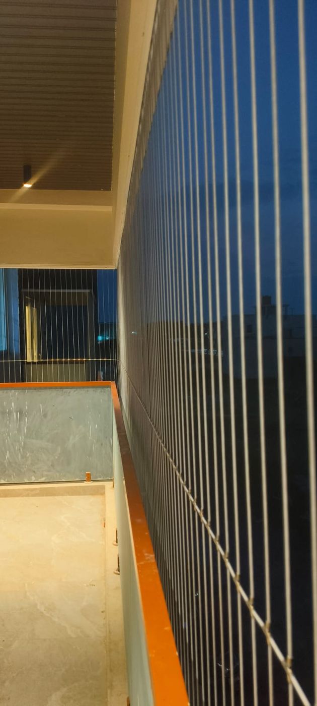 Vertical invisible grill cables along a lit balcony with orange-edged parapet at dusk.
