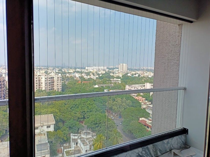 High-rise balcony opening secured with vertical invisible grills, overlooking leafy streets and a sprawling city skyline.