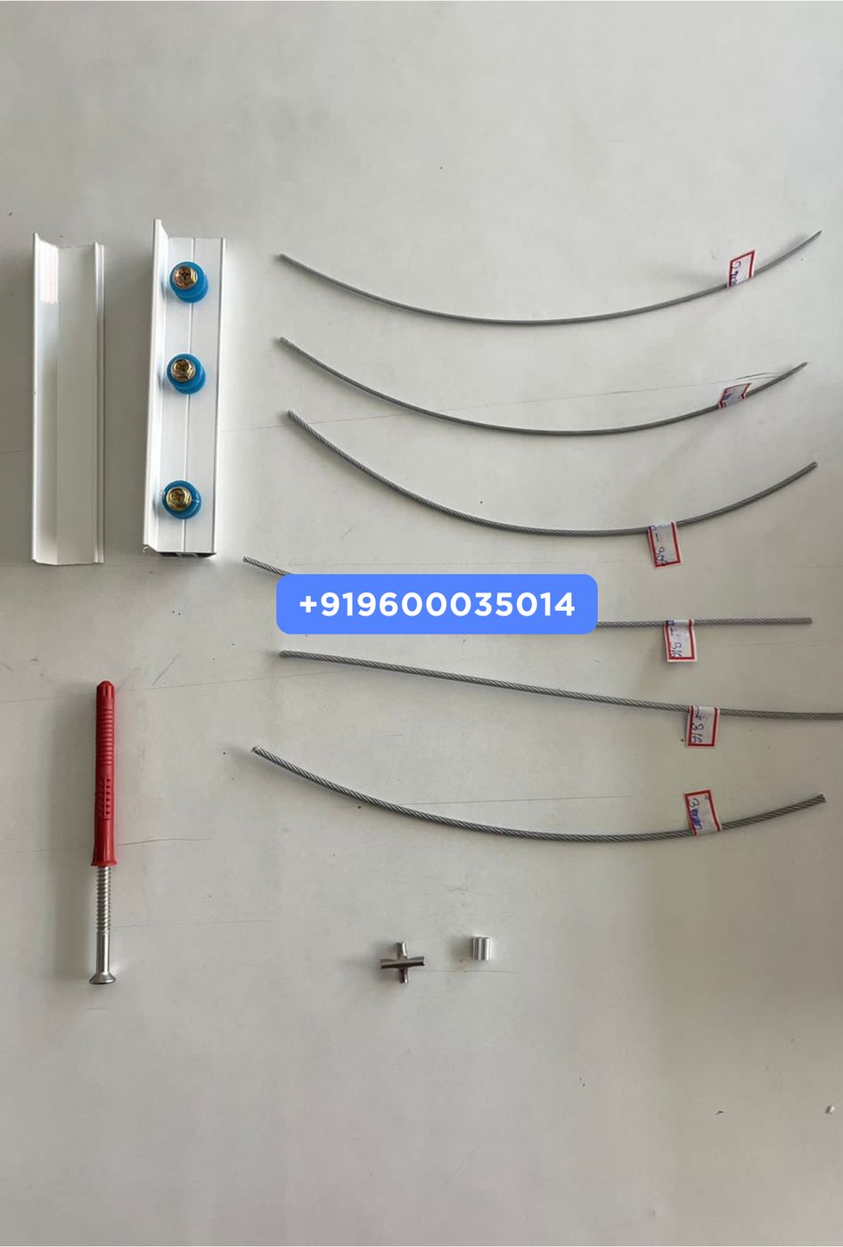 Invisible grill cable samples, mounting channels, fasteners, and a red-handled tool arranged on a light surface.