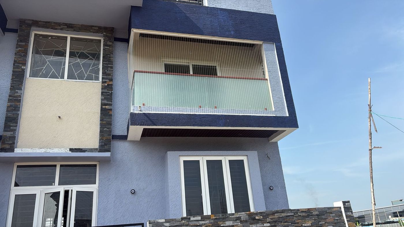 Exterior of a blue-and-white house with vertical invisible grills enclosing an upper balcony above frosted glass railing panels.