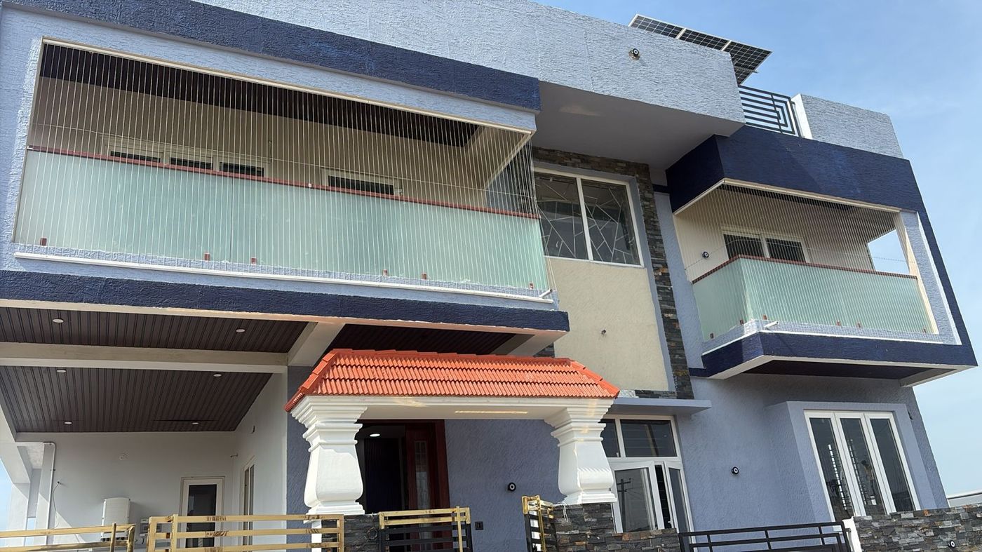 Two-storey villa exterior with invisible grills enclosing an upper balcony above frosted glass railings.
