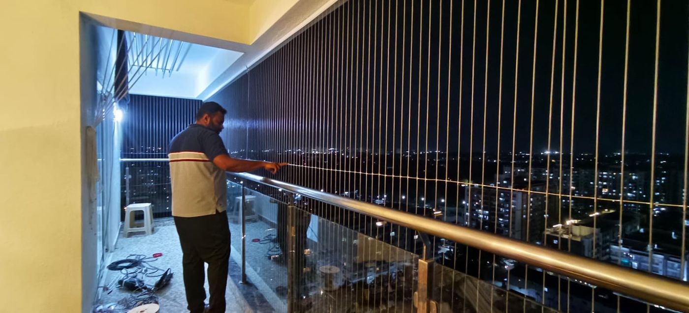 Installer working on vertical invisible grills along a high-rise balcony at night, with city lights beyond.