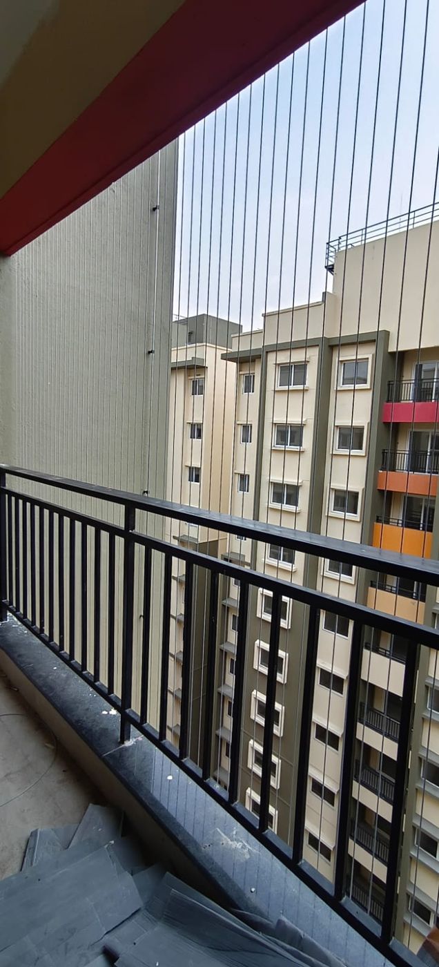 Balcony with vertical invisible grills and black metal railing facing a neighboring apartment building.