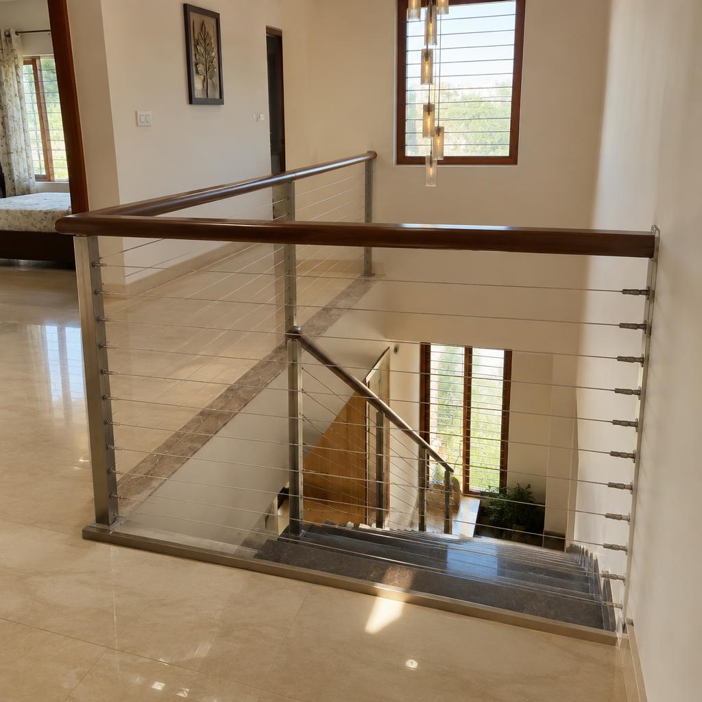 Horizontal stainless steel invisible grill wires fitted across a duplex home staircase opening with a wooden handrail