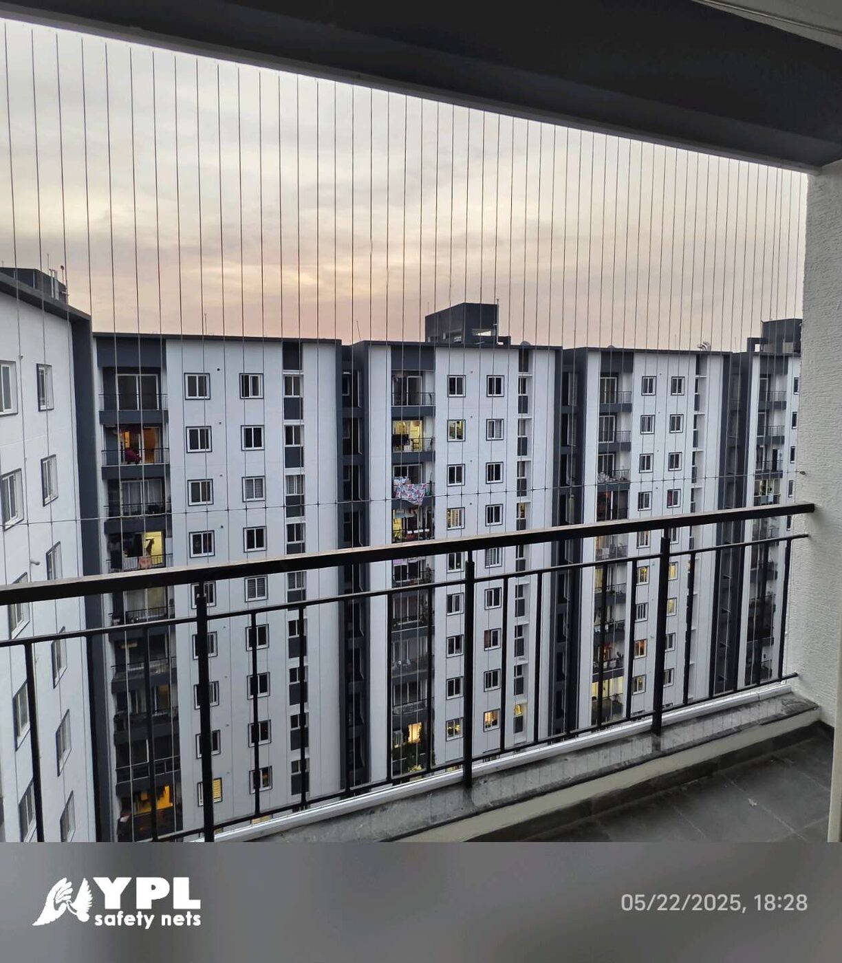 Balcony with vertical invisible grills and black railing overlooking neighboring apartment towers at dusk.
