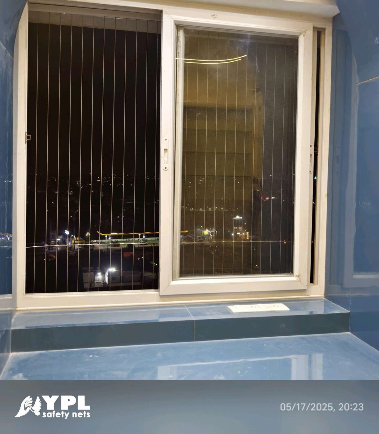 White sliding window with vertical invisible grills, blue interior walls, and city lights visible at night.