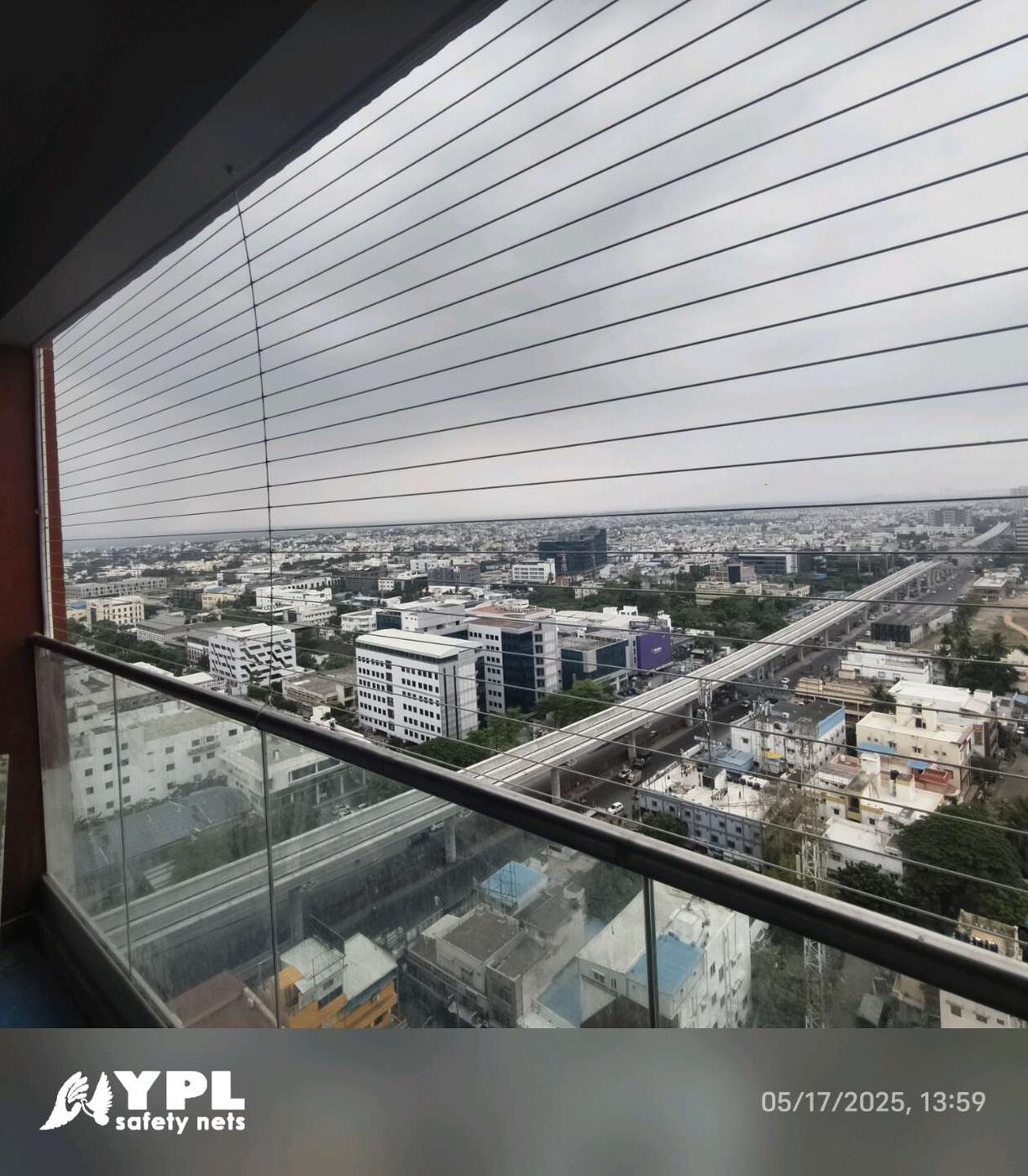 High-rise balcony with horizontal invisible grills, glass railing, and expansive city views overlooking an elevated roadway.