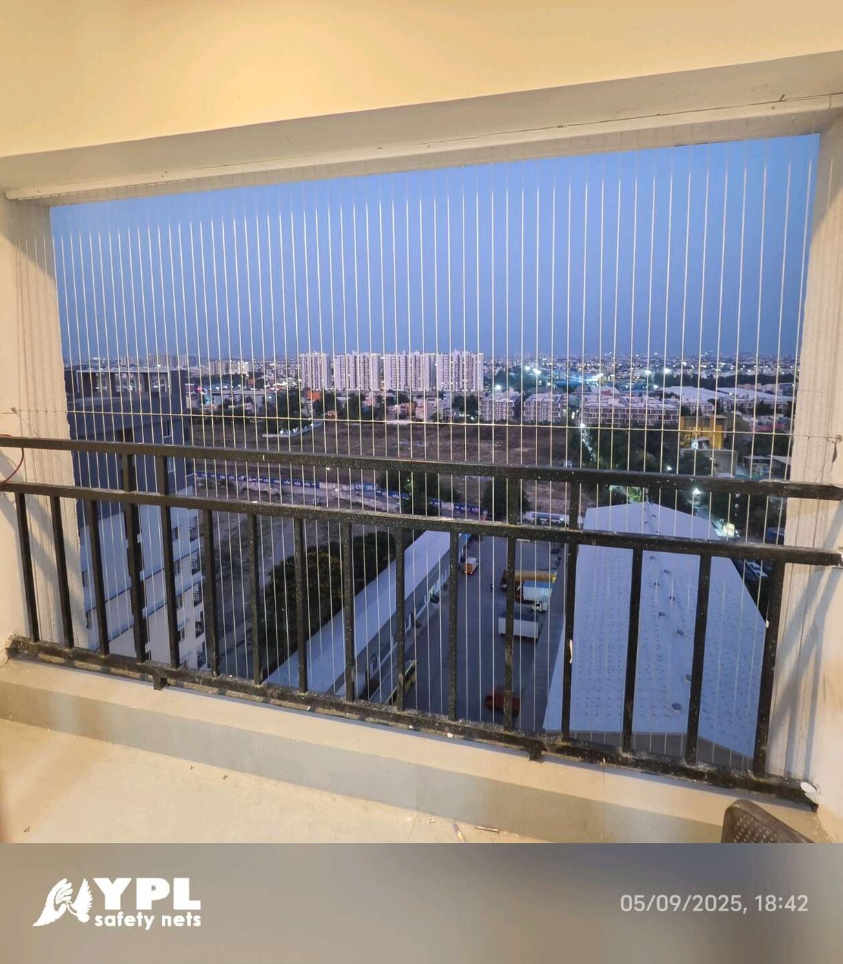 Front view of a balcony opening fitted with vertical invisible grills, overlooking rooftops and distant apartments at dusk.