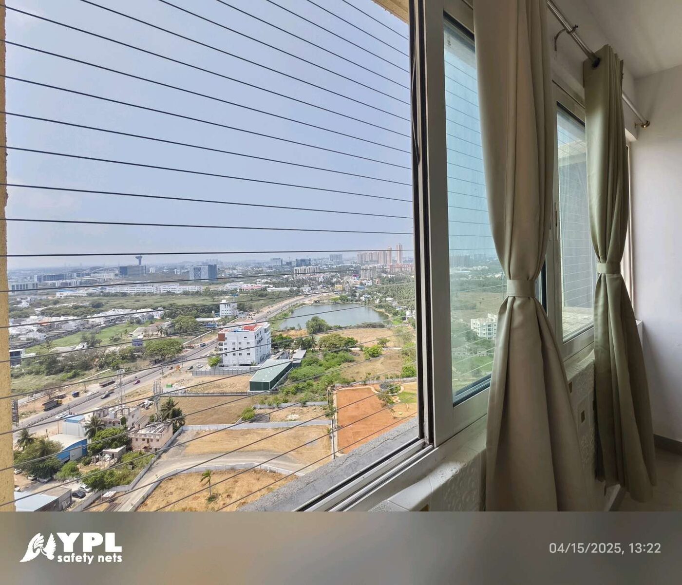 Curtained sliding windows with horizontal invisible grills overlooking roads, greenery, and distant buildings from a high-rise apartment.