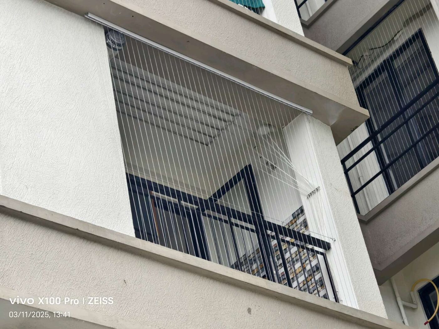 Upward exterior view of an apartment balcony enclosed with vertical invisible grill wires above black railings.